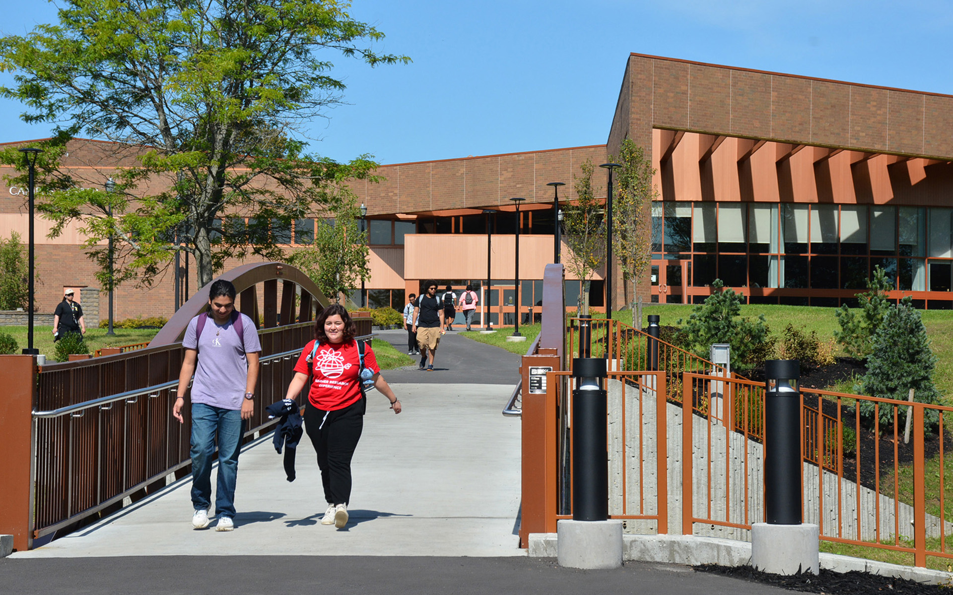 students walking over the new bridge on the Utica campus