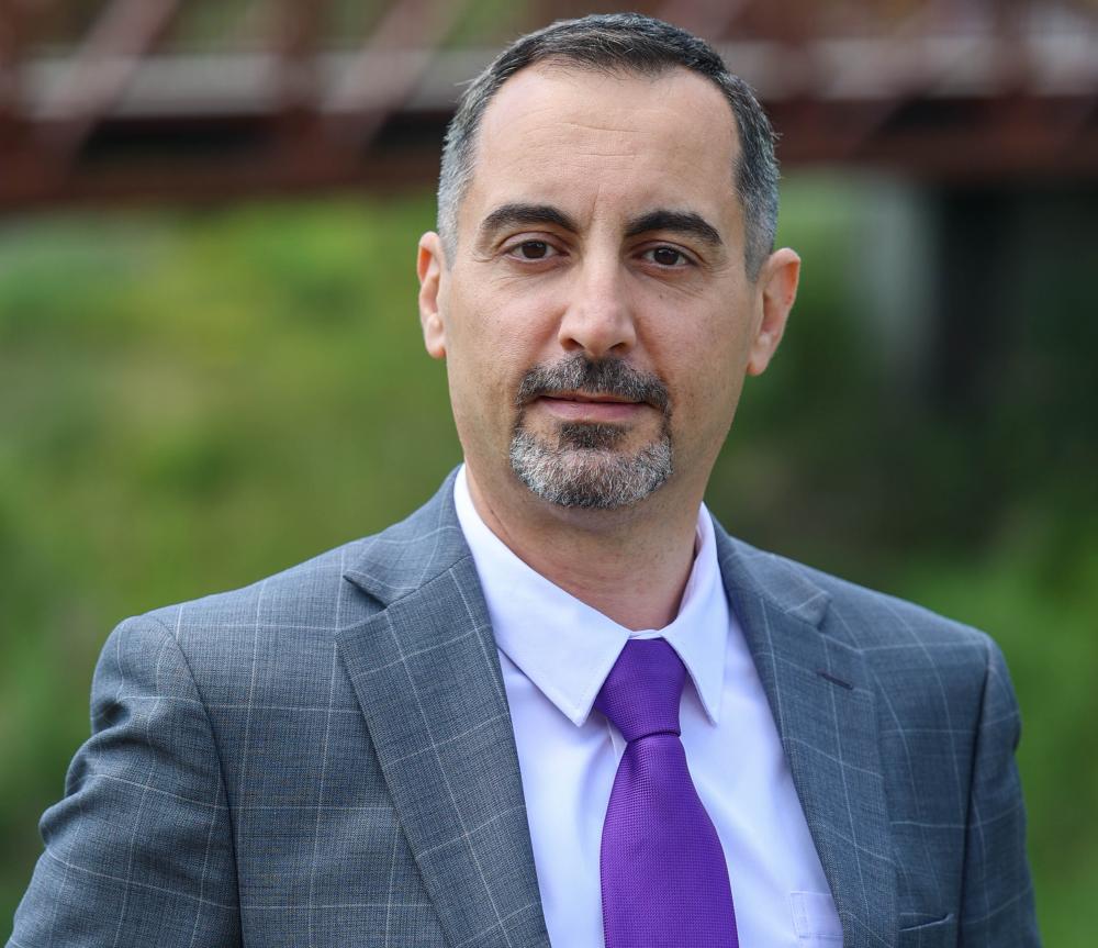 Dr. Yasser Alhenawi in a blazer with white dress shirt and purple tie.