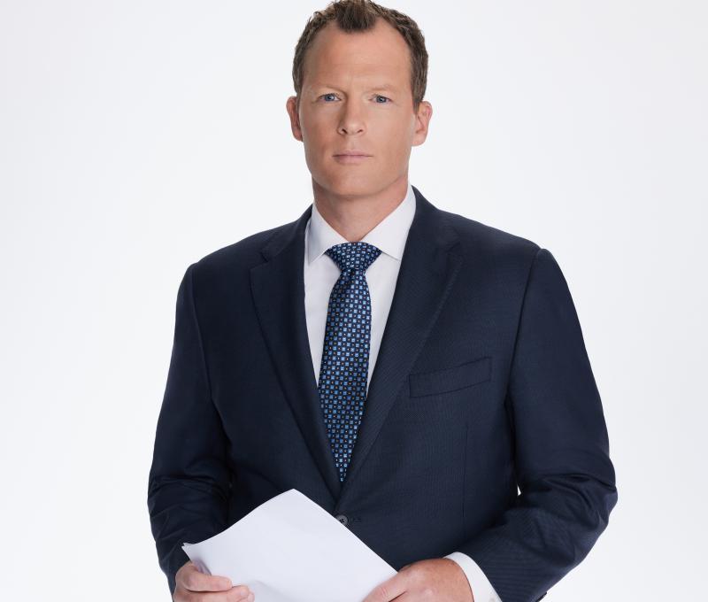 Ryan Nobles headshot. He is wearing full suit, holding paper.